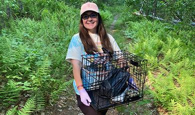 While walking in the woods, Sarah Calis holds a crate used for her research.